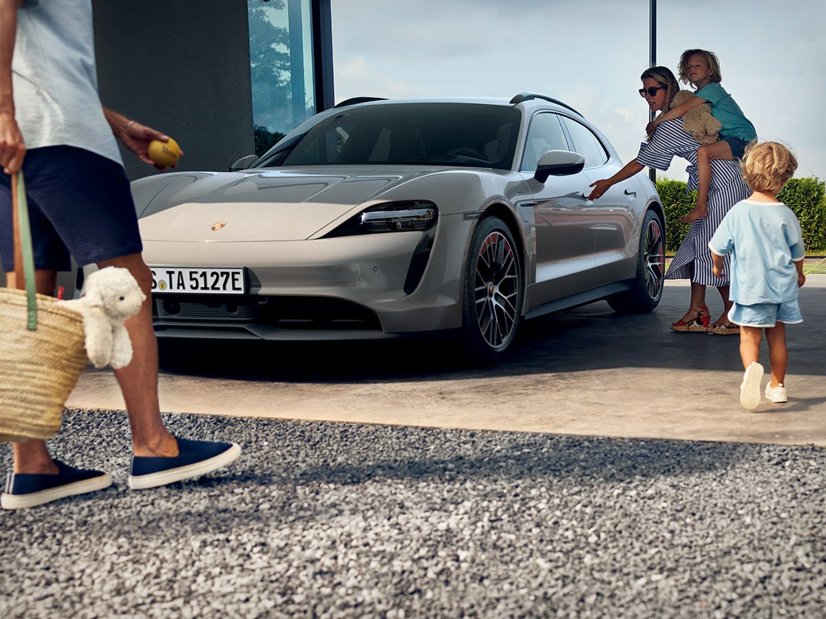 Eine Mutter mit einem Kind auf dem Rücken öffnet die Vordertür des Porsche Taycan.