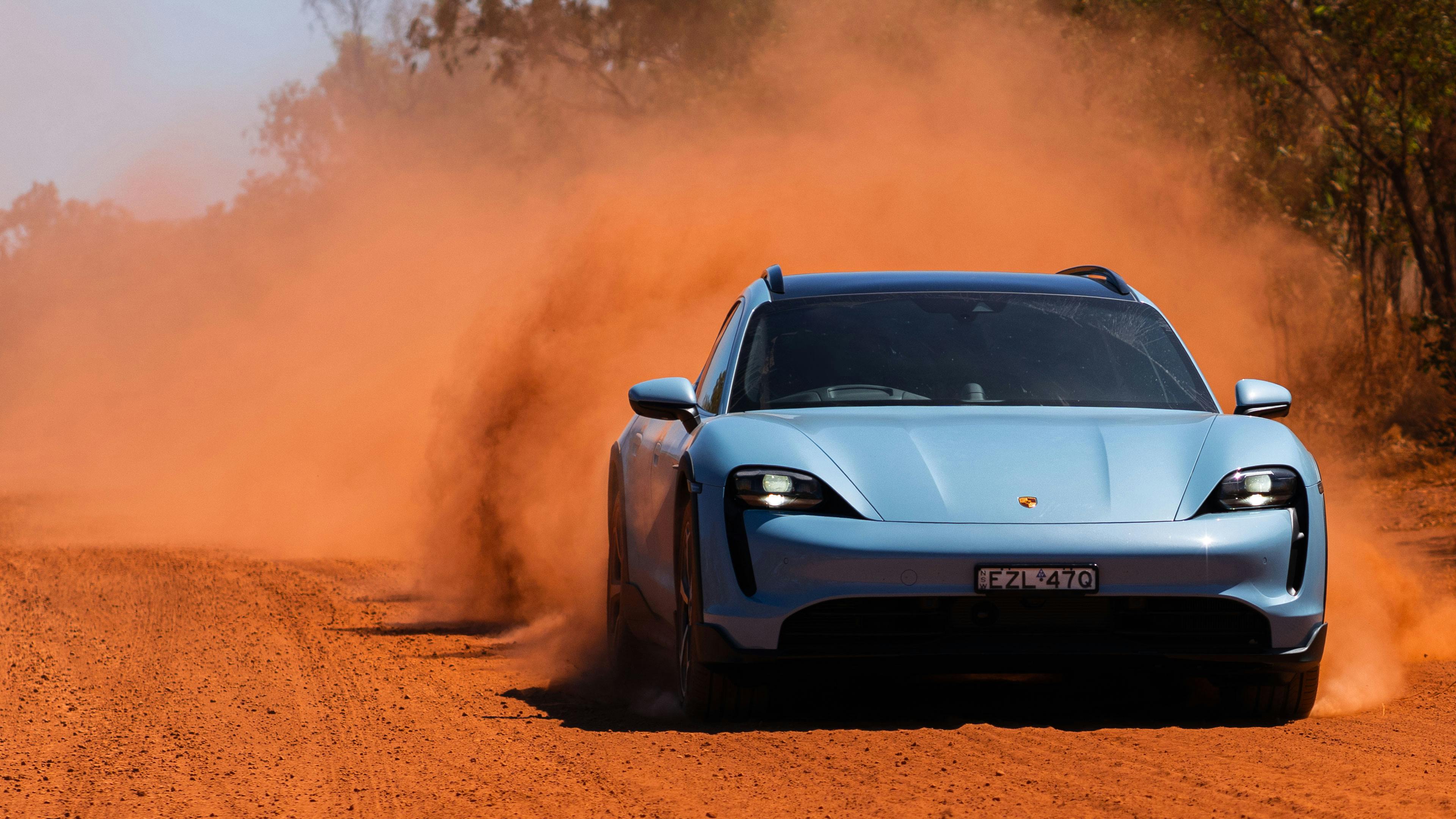 Porsche Taycan 4S driving on a dry dirt road with red dust trailing