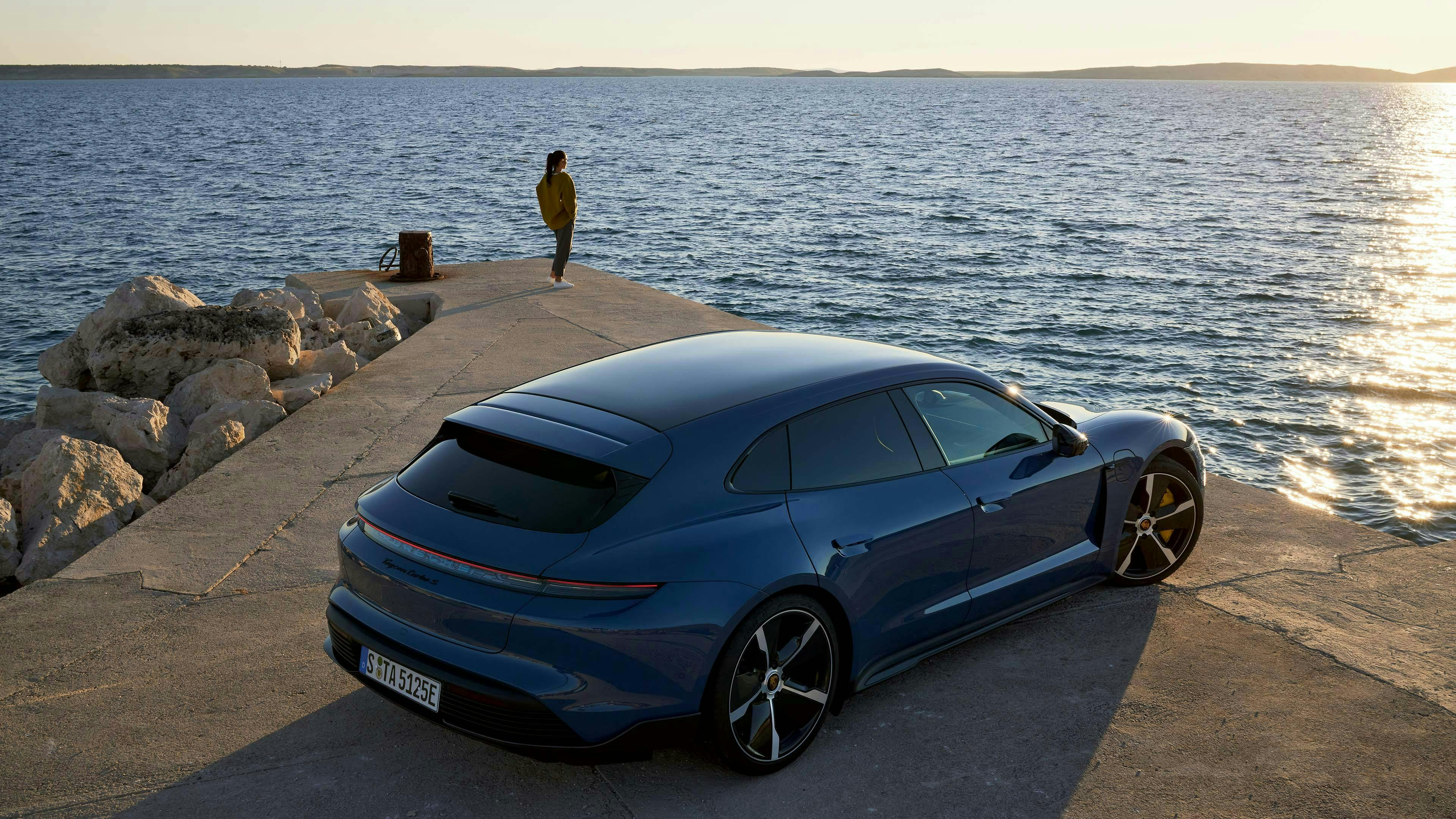 Turbo S Sport Turismo in the foreground with a woman looking toward an ocean sunset