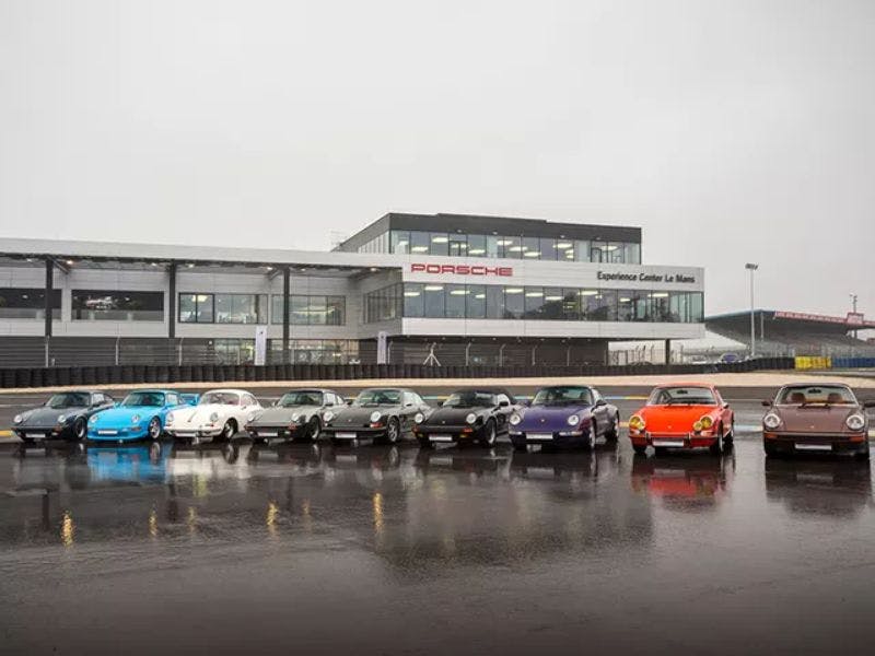 Les neuf voitures restaurées sont placées côte à côte devant le Porsche Experience Center Le Mans.