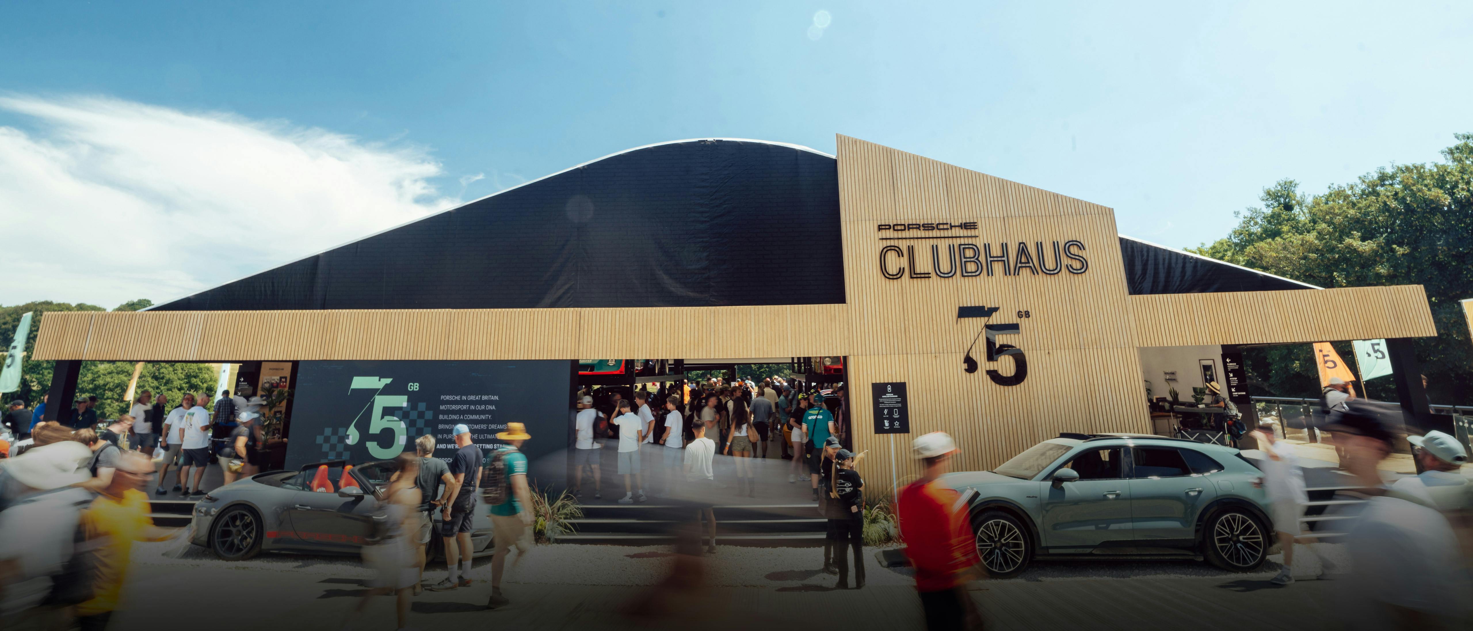 Porsche Clubhaus exterior at Goodwood Festival of Speed, marking 75 years of Porsche in the UK, with visitors and a Porsche parked outside.