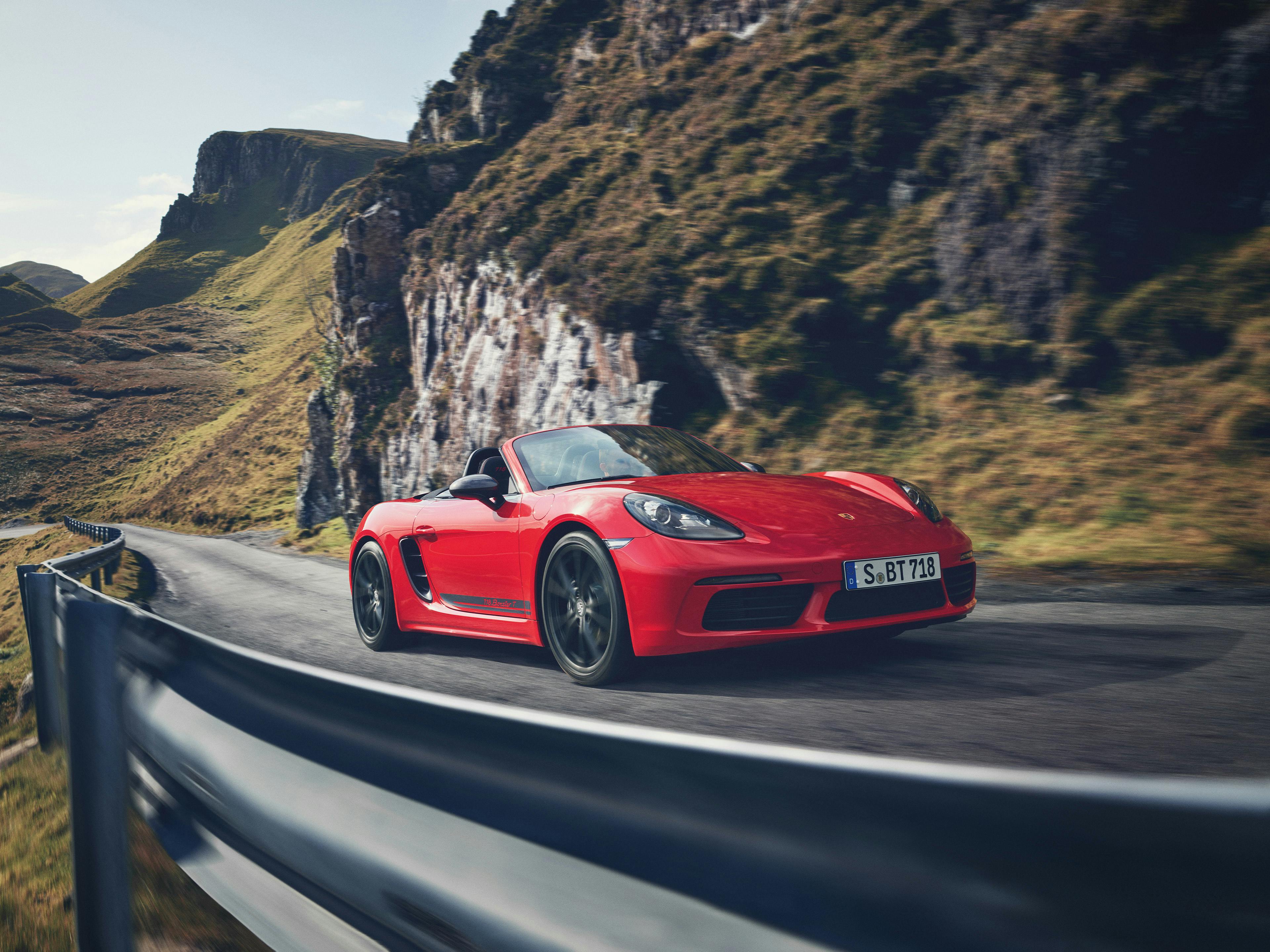 Ein roter Porsche Boxster fährt auf einer kurvigen Gebirgsstraße.