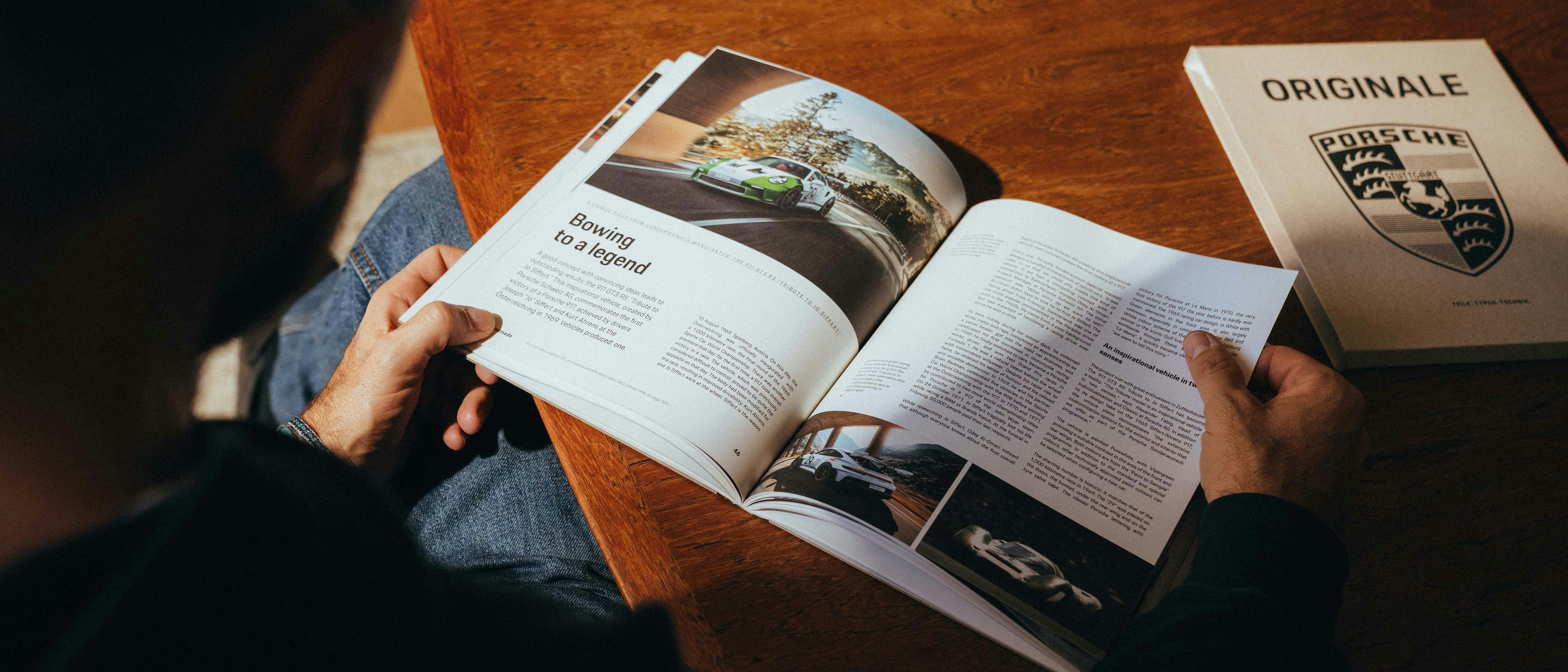 Andrea Vailetti sits at a table in a café with a copy of ORIGINALE 11. On the table are an espresso, a croissant, and a camera.