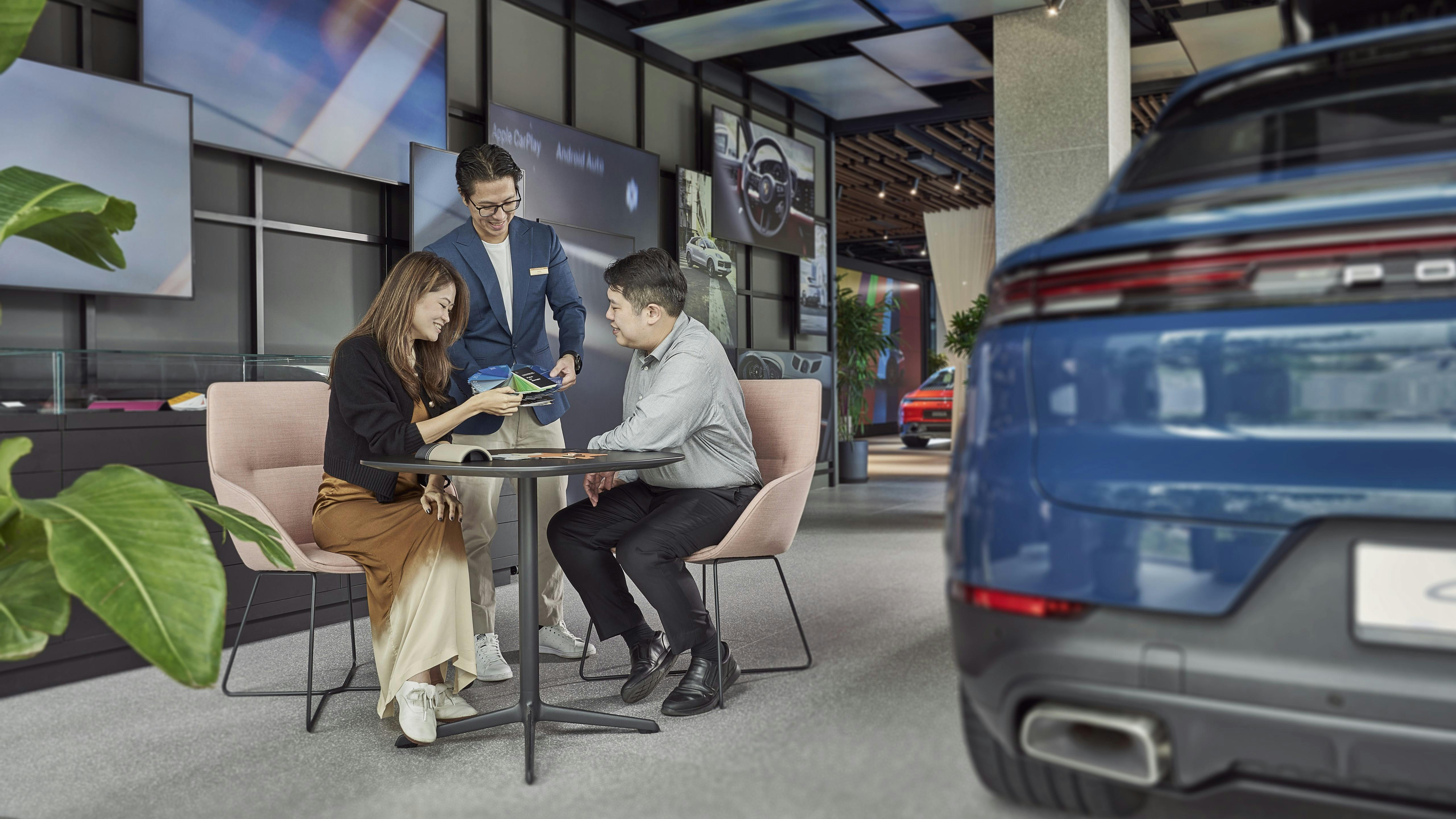 Customers configuring a vehicle at Porsche Studio Singapore, assisted by a Porsche Pro displaying a Paint to Sample colour swatch.