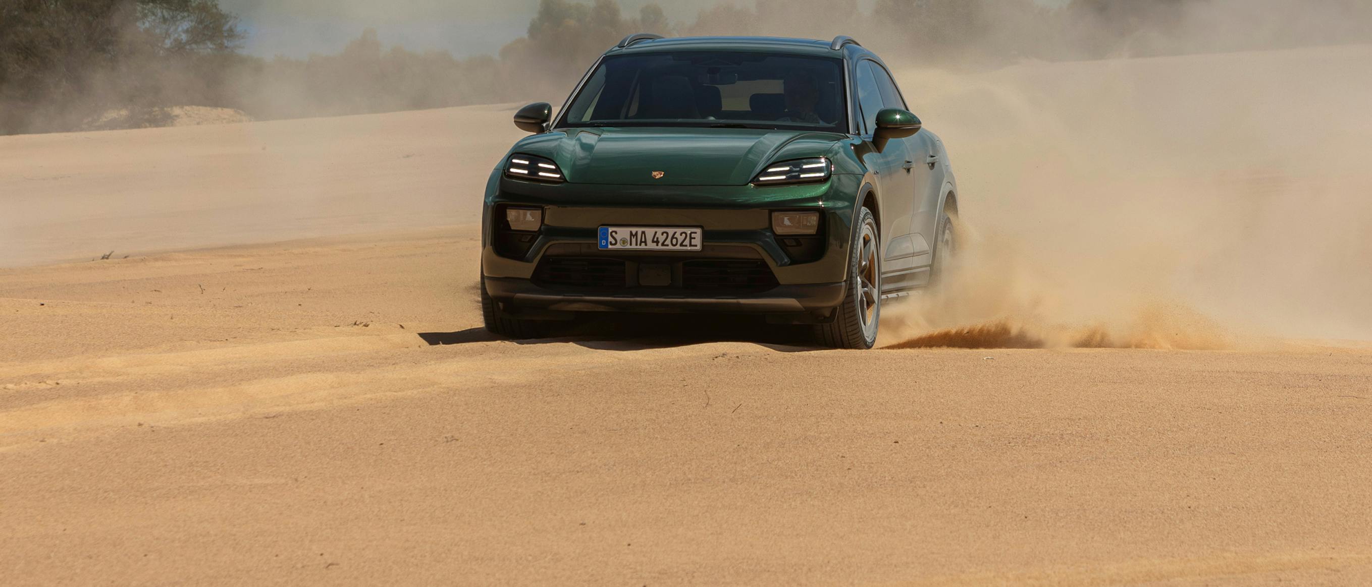 Um Porsche Macan 4S a circular sobre areia e a levantar poeira. Vista frontal da frente.