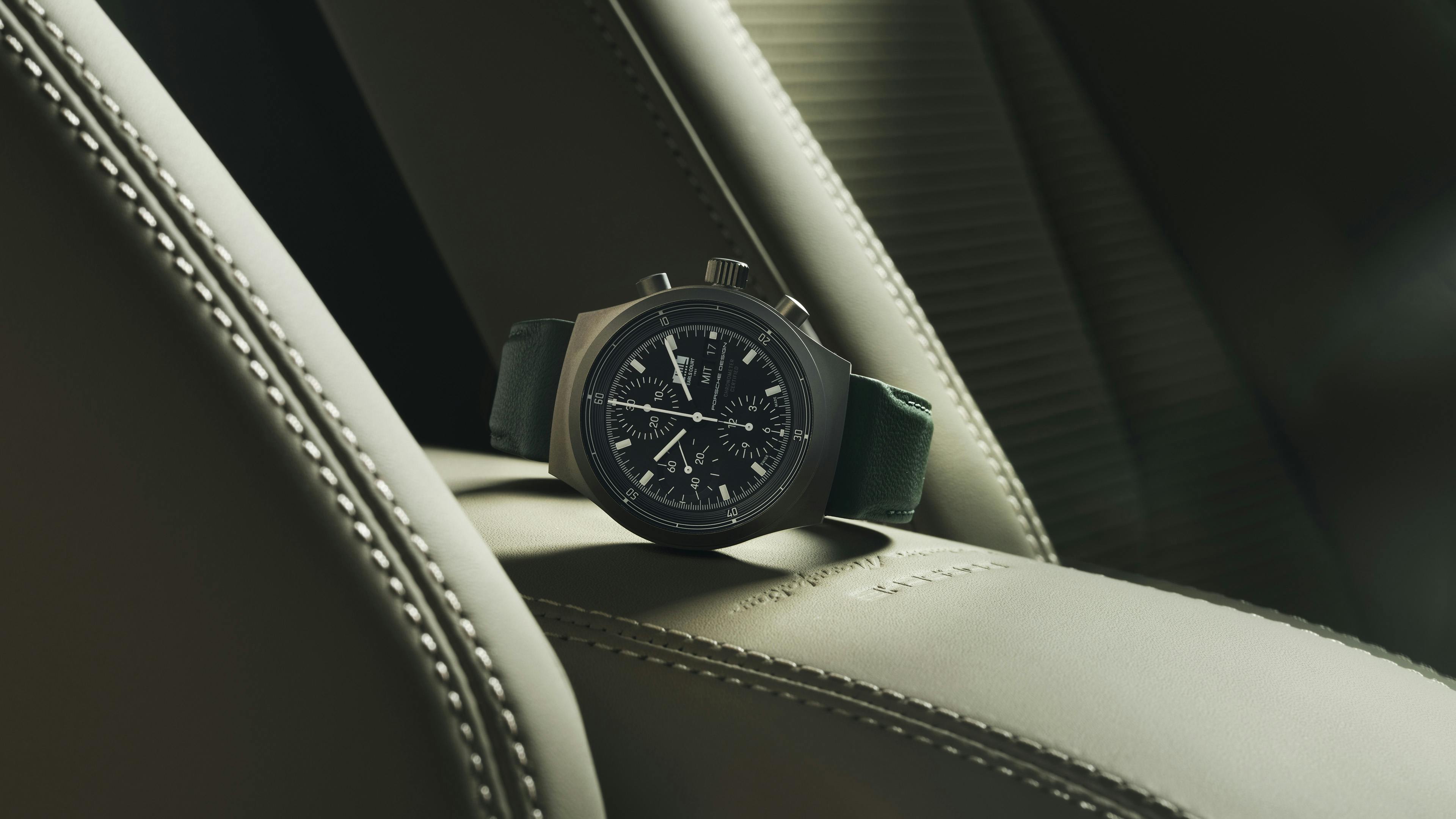 A Porsche Design chronograph watch with a dark dial resting on a cream leather seat.​