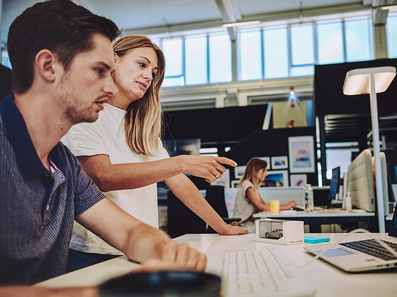 Two doctoral students at Porsche sit at a desk and discuss.