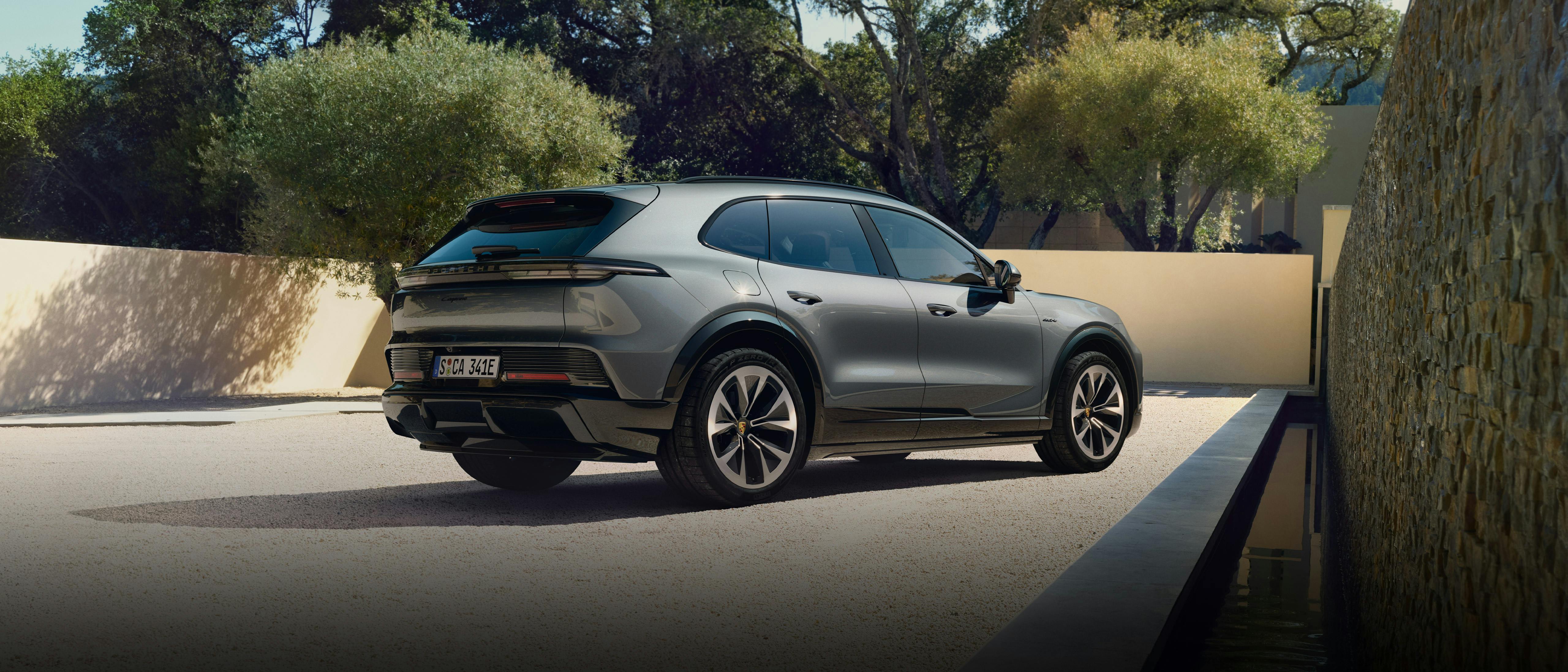 The Cayenne Electric SUV parked on a light coloured pebble ground while facing the wall, there are trees in the background.