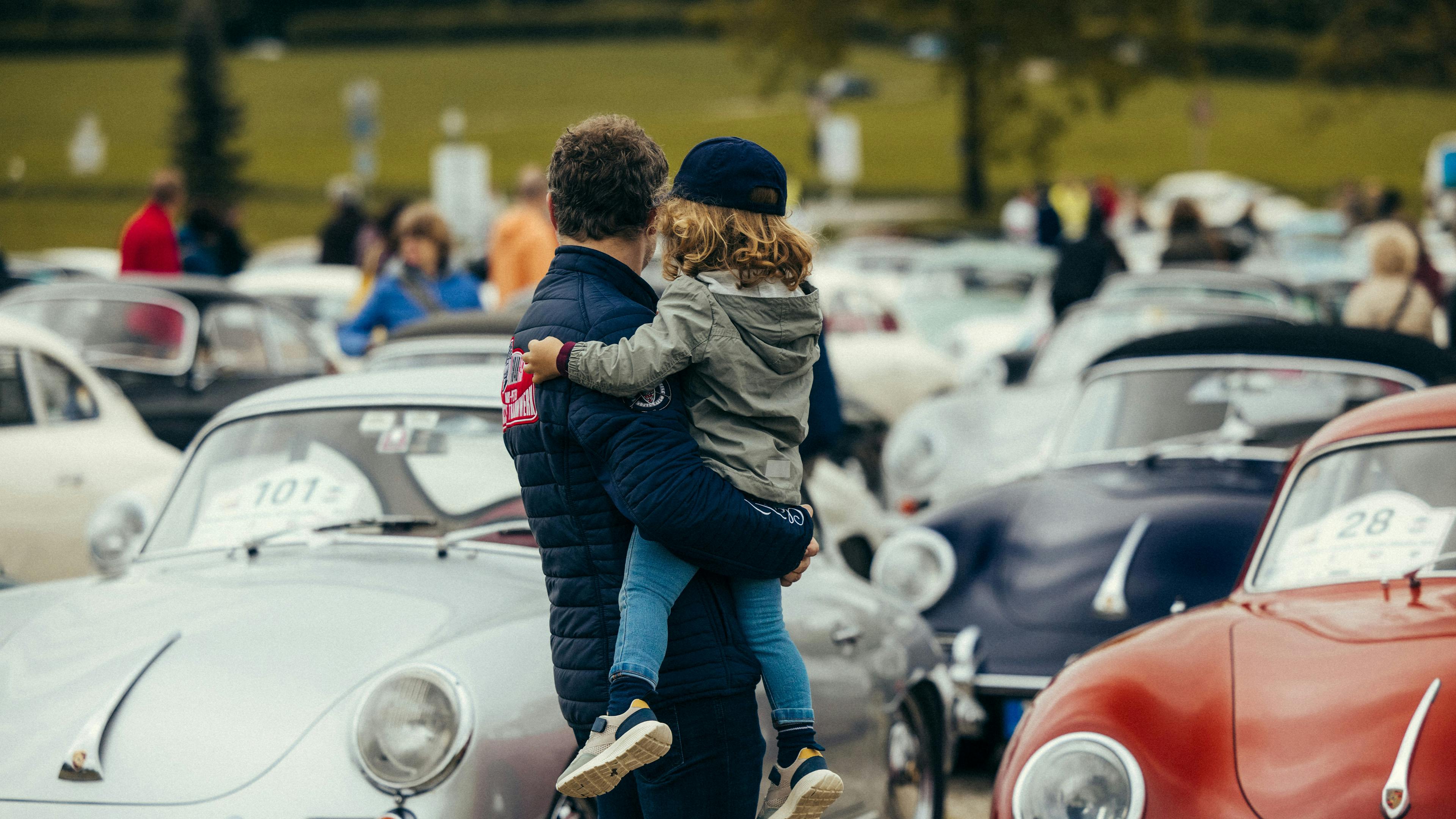 A man carrying a child at a Porsche event.