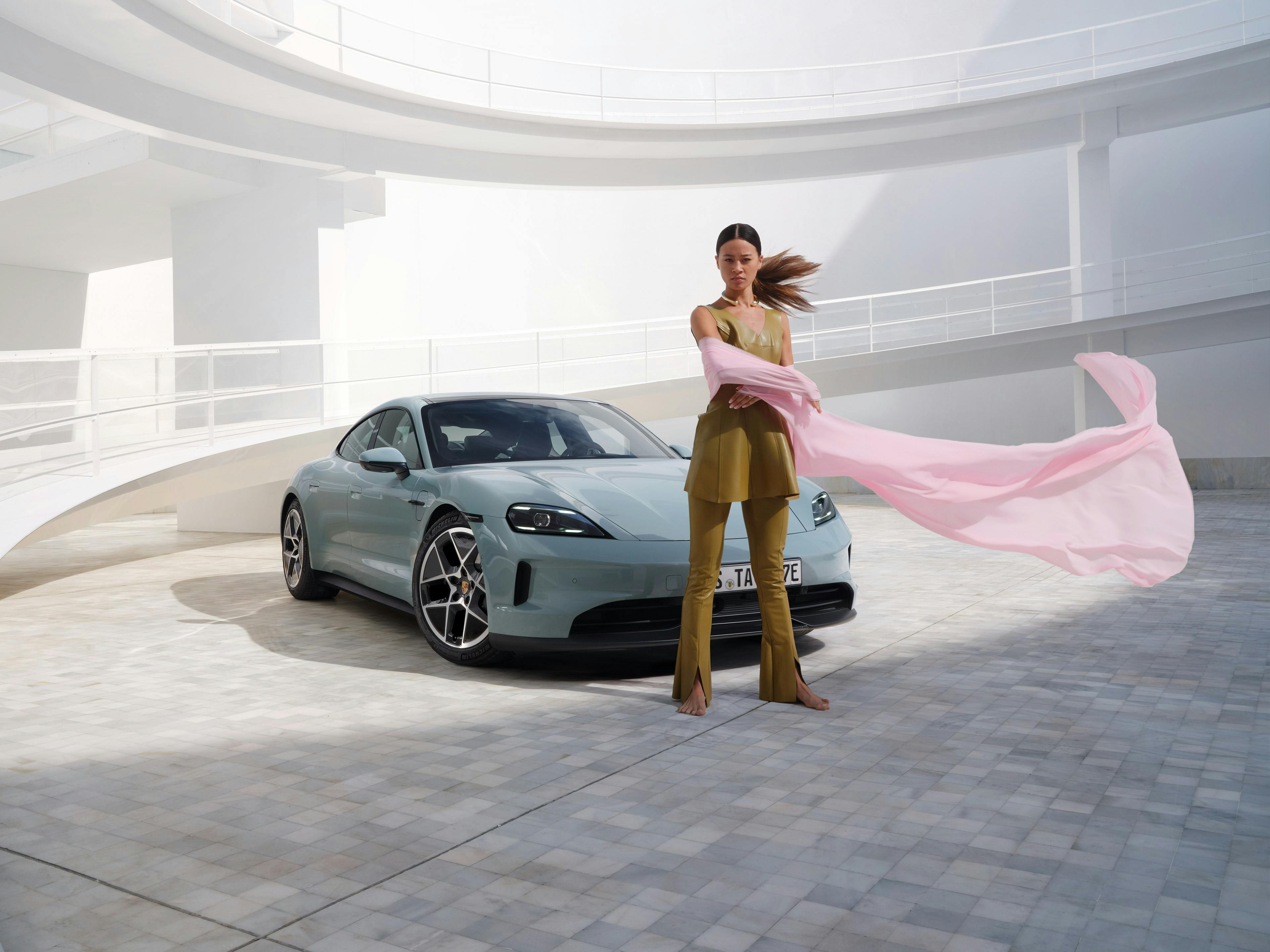 A woman waving a piece of clothing while stood in front of the new all-electric Taycan.