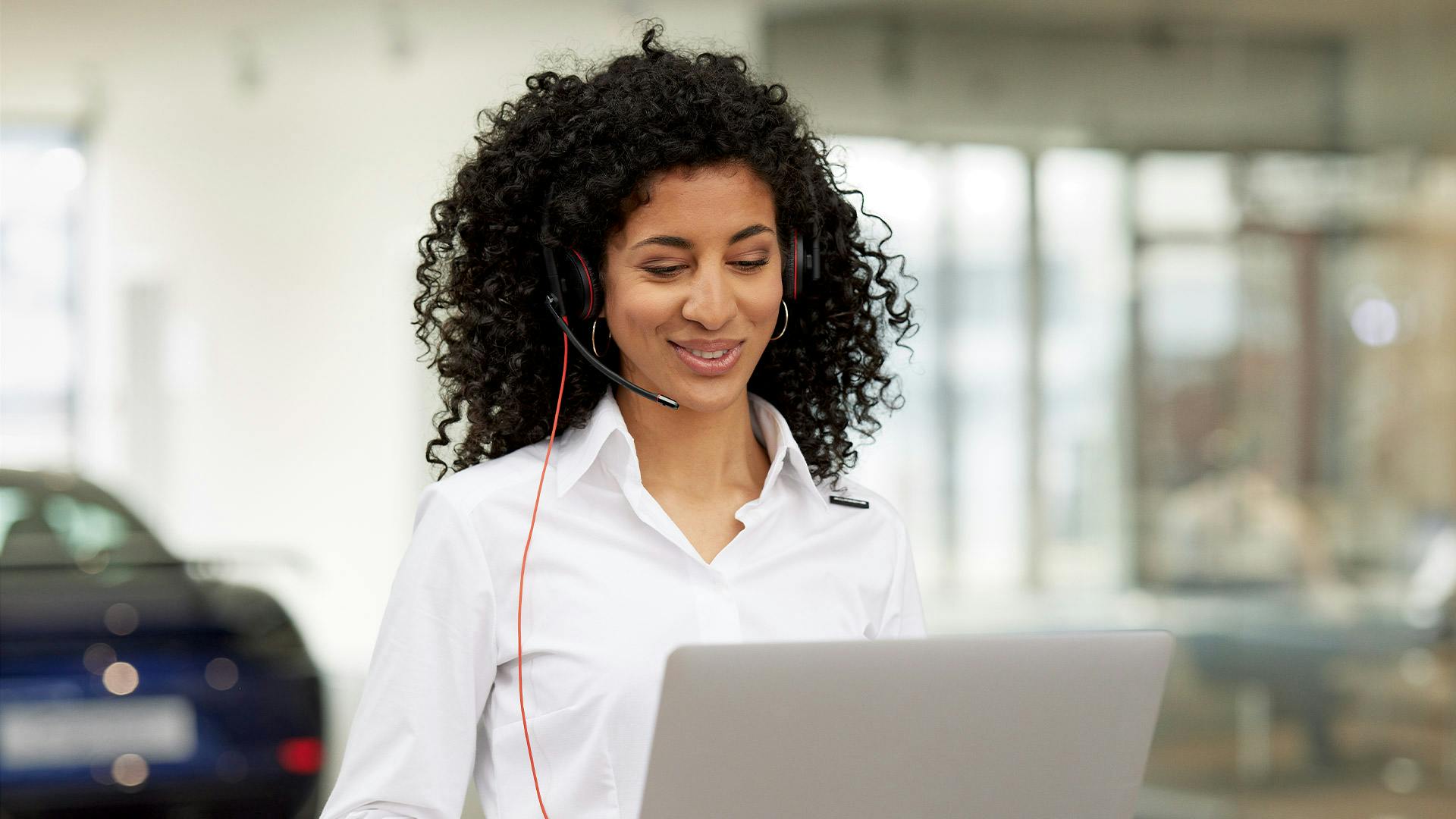 A Porsche service assistant is in a conversation via headphones and looking at her laptop.