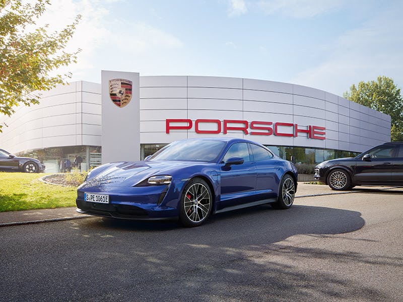 Ein blauer Porsche steht vor einem Porsche Gebäude.