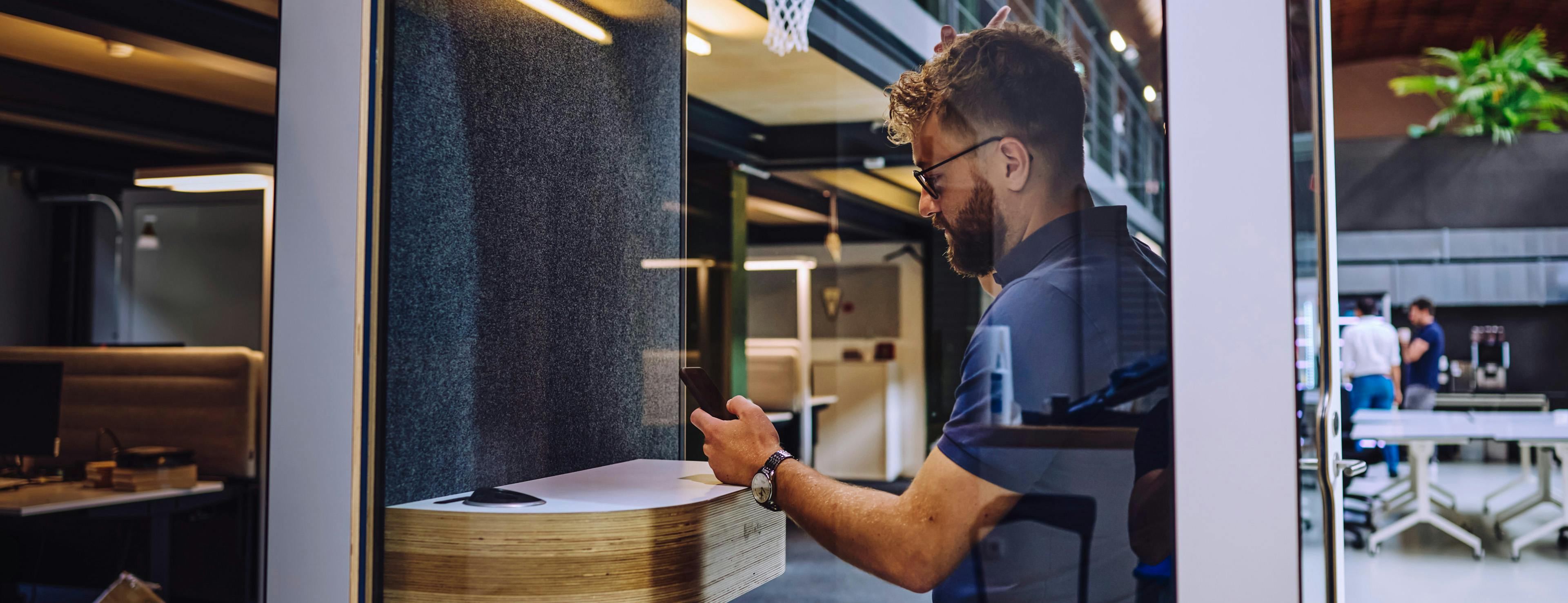 An office at Porsche: a man is sitting in a phone booth, typing intently on his mobile phone.