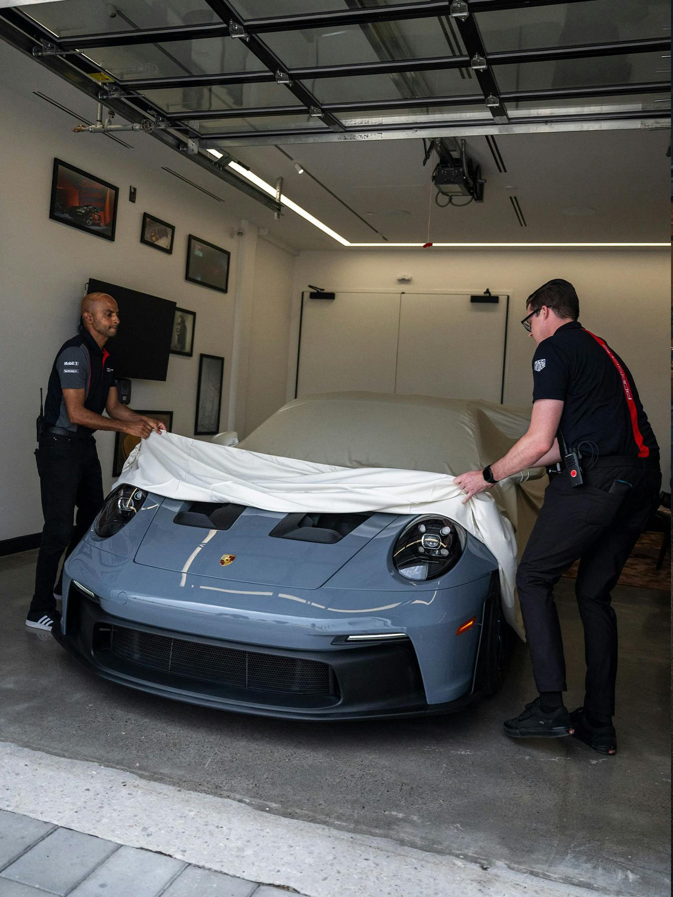 A grey Porsche 911 GT3 RS being revealed as its car cover is gently pulled away.