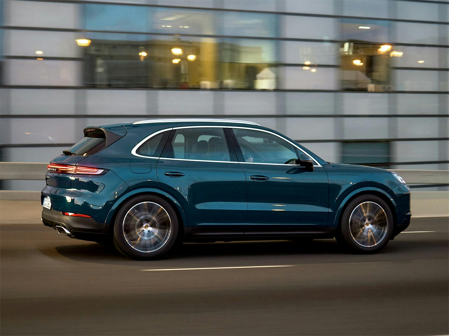 A blue Porsche Cayenne driving through the city streets in the evening.